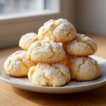 A tempting stack of soft, pale yellow 3-ingredient butter cookies dusted generously with white powdered sugar.