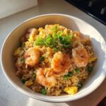A close-up overhead shot of a white bowl filled with flavorful shrimp fried rice, topped with large shrimp and green onions.