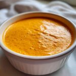 A close-up of rich, orange beer cheese dip served warm in a white ramekin dish.