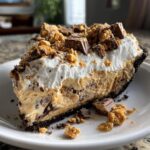 A generous slice of no-bake butterfinger pie with a chocolate crust, peanut butter filling, whipped cream, and Butterfinger candy pieces.
