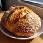 A beautifully baked, round loaf of italian bread with a golden, crackly crust dusted with flour.