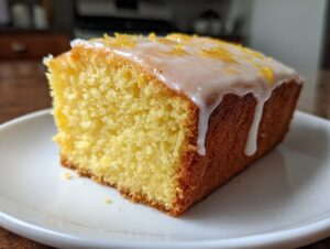A close-up of a moist slice of amazing lemon pound cake topped with white glaze and zest.
