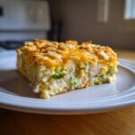 A square serving of creamy chicken and broccoli rice casserole topped with melted cheddar cheese and crispy crumbs.