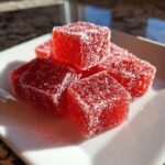 A small pile of bright red, sugar-coated Candy Cane Fireball Gummies resting on a white square plate.