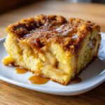 Close-up of a moist slice of caramel apple dump cake topped with rich caramel sauce.