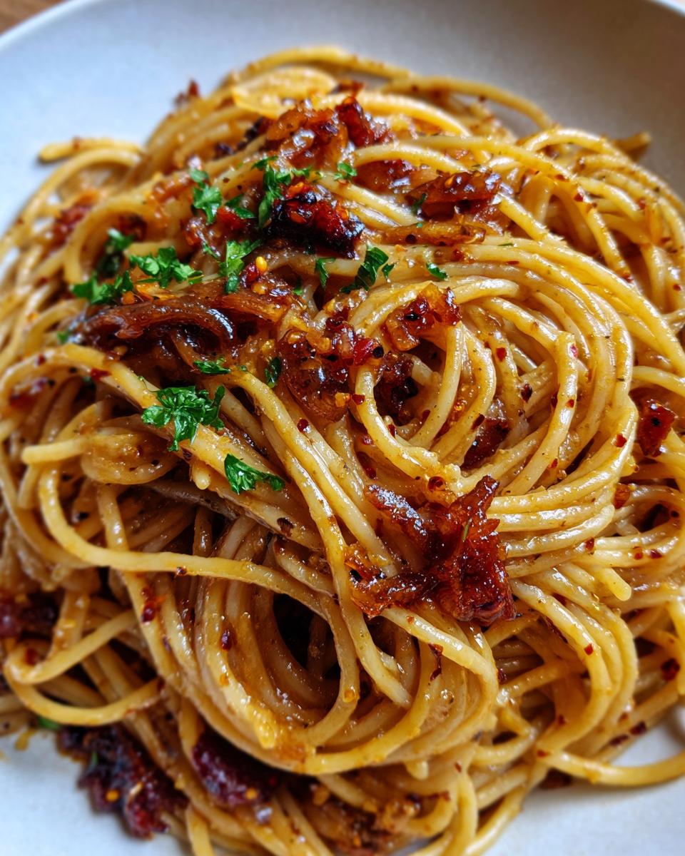 A close-up shot of a serving of caramelized onion pasta, topped with dark caramelized onions and fresh parsley.