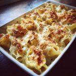 Close-up of baked chicken alfredo stuffed shells bubbling in a white dish with a golden, cheesy crust.