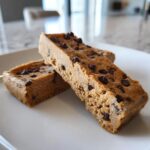 Two rectangular, dense chocolate chip protein bars resting on a white plate.