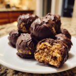 A pile of chocolate-covered pecan pie balls, one cut open showing the textured, nutty interior.