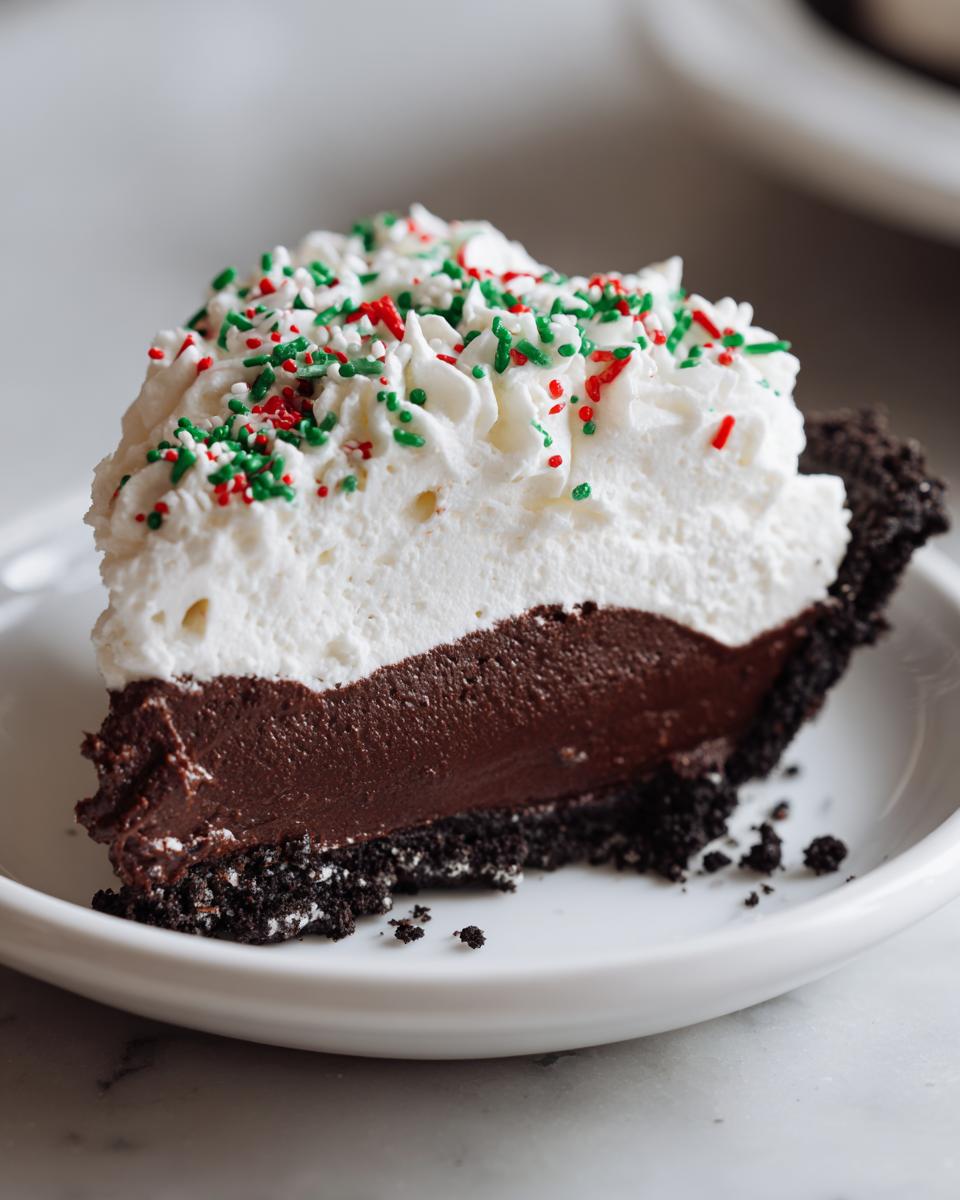 A decadent slice of Christmas chocolate cream pie featuring a dark chocolate filling, whipped cream topping, and red and green holiday sprinkles.
