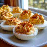 Close-up of several perfectly piped deviled eggs sprinkled with paprika on a light plate.