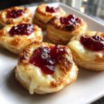 Close-up of baked cranberry brie bites featuring melted brie, red cranberry topping, and flaky pastry.