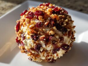A close-up of a perfectly formed cranberry pecan cheese ball coated in dried cranberries and chopped pecans.