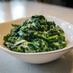 Close-up of rich, vibrant green creamed spinach recipe mixed with a creamy white sauce in a white serving bowl.