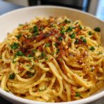 Close-up of creamy caramelized onion pasta topped with fresh parsley and chili flakes in a white bowl.
