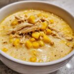 Close-up of a bowl of creamy chicken corn chowder topped with shredded chicken and whole corn kernels.
