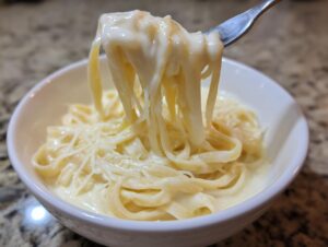 Close-up of fettuccine noodles being lifted from a bowl, coated in rich homemade alfredo sauce.