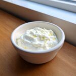 A small white bowl filled with creamy, white garlic aioli, topped with lemon zest.