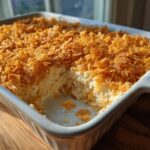 A creamy hashbrown casserole in a white baking dish with a thick, crunchy cornflake topping.
