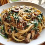 Close-up of creamy mushroom pasta featuring fettuccine, sautéed mushrooms, and wilted spinach, topped with Parmesan.