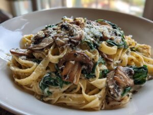 Close-up of creamy mushroom pasta featuring fettuccine noodles, sautéed mushrooms, spinach, and grated Parmesan cheese.