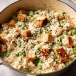 Close-up of creamy one pot chicken and rice dish topped with peas, chicken pieces, and grated Parmesan.