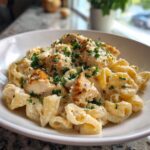 Close-up of creamy chicken pasta topped with grilled chicken pieces and fresh parsley.