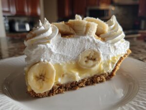 A close-up of a generous slice of banana cream pie showing the graham cracker crust, creamy filling, and whipped topping with banana slices.