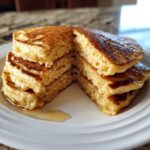 Close-up of a stack of fluffy banana oatmeal pancakes, cut to show the texture, drizzled with syrup.
