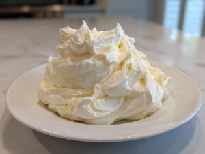 A generous mound of freshly piped, fluffy cream cheese frosting sitting on a white plate.