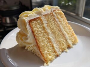 A close-up of a moist slice from a vanilla cake recipe showing three layers of cake and white frosting.