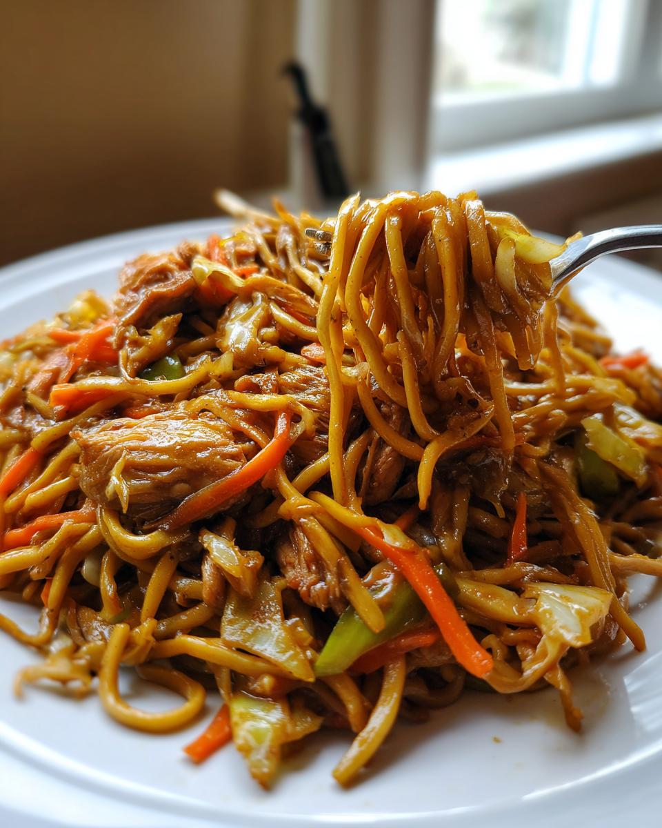 A fork lifting noodles, chicken, and vegetables from a plate of homemade chicken chow mein recipe.