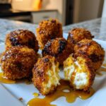 Close-up of crispy fried goat cheese balls, one cut open revealing creamy white cheese, drizzled with honey.