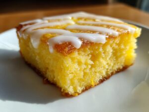 A close-up shot of a square slice of bright yellow, fudgy lemon brownies topped with white lemon glaze.