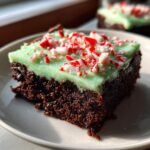 Close-up of a fudgy peppermint brownie slice topped with bright green mint frosting and crushed candy canes.