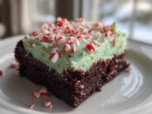 A close-up of a fudgy peppermint brownie square topped with light green mint frosting and crushed candy canes.