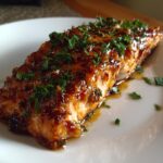 Close-up of a perfectly cooked salmon fillet covered in a shiny, dark glaze and topped with chopped fresh parsley.