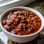 Close-up of a white bowl filled with rich, thick crockpot chili featuring ground beef and kidney beans.