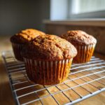Three freshly baked honey bran muffins cooling on a wire rack with a wooden surface underneath.