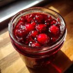 Close-up of a glass jar filled with vibrant, whole-berry christmas jam, likely cranberry or cherry.