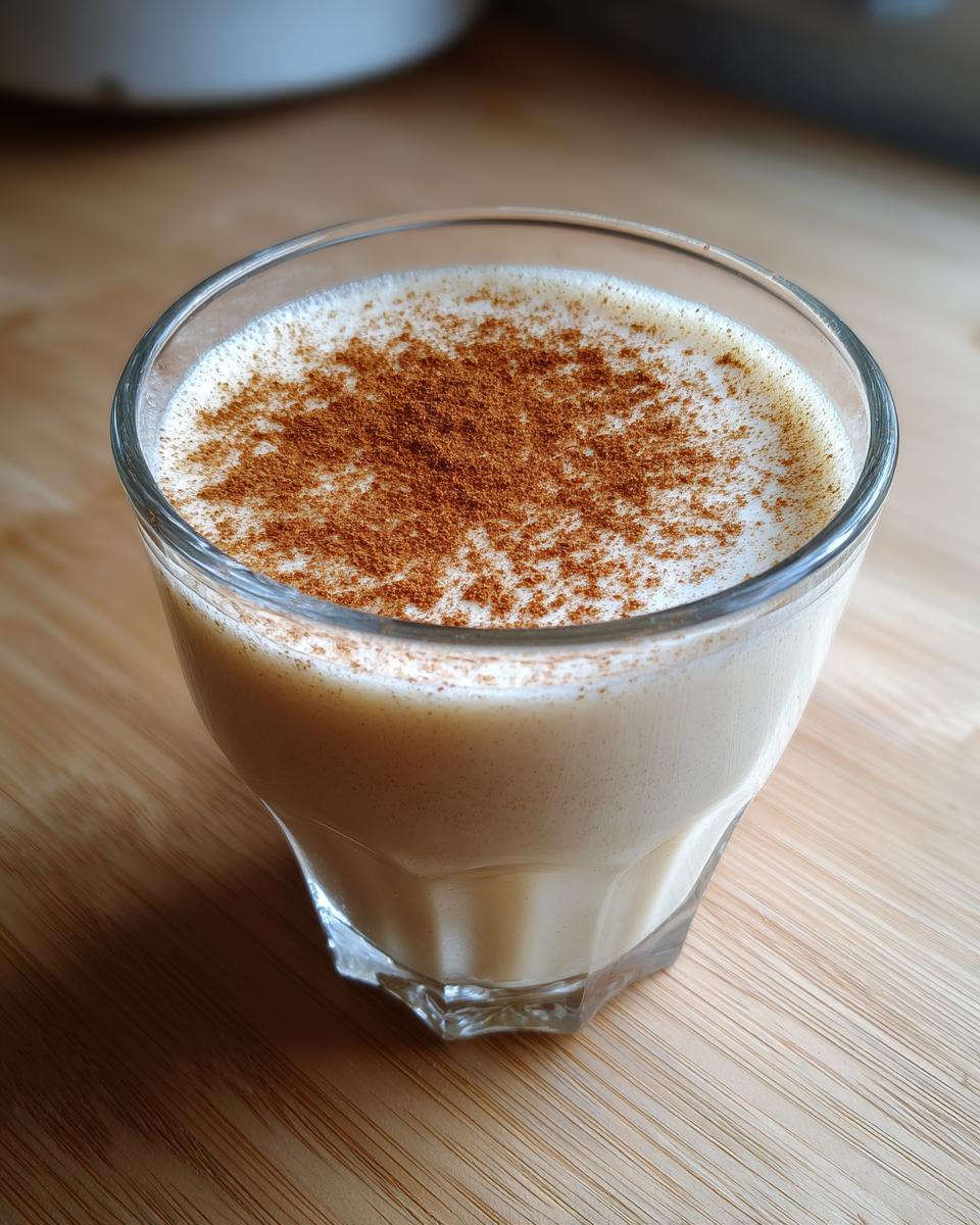 A glass of creamy, light-colored coquito topped generously with ground cinnamon.