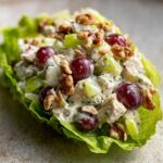 Close-up of a creamy Waldorf salad filling served in a crisp lettuce cup, topped with red grapes and walnuts.