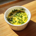 Close-up of melted cowboy butter dipping sauce, bright yellow with fresh green parsley, in a white ramekin.