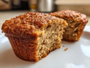 Close-up of a moist bran muffin cut in half showing the soft interior texture, with another muffin blurred in the background.