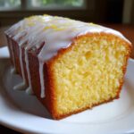 A close-up of a slice of moist lemon pound cake topped with white glaze and lemon zest.