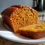 A close-up view showing the texture of moist pumpkin bread, with one slice cut and resting beside the main loaf.