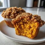 Close-up of a moist sweet potato muffin cut in half, showing the bright orange interior and cinnamon streusel topping.