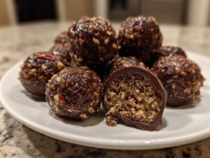 A plate of decadent, chocolate-coated pecan pie balls, one cut open to show the textured, nutty interior.