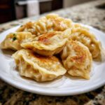 A close-up of several pan-fried Traditional Chinese Dumplings piled on a white plate, showing golden-brown bottoms.