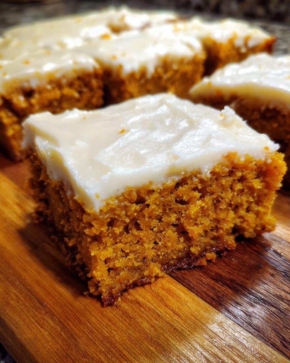 A thick, moist square of pumpkin bars with cream cheese frosting sitting on a wooden cutting board.
